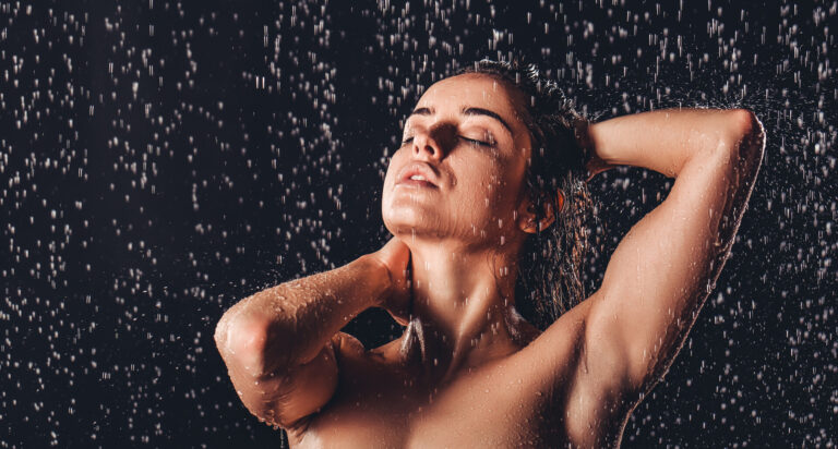 Sexy woman in shower. Attractive young naked woman under water drops isolated on black background.